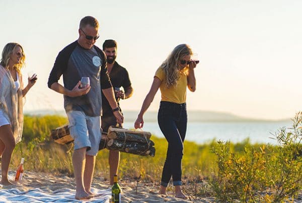 Four individuals walking on beach enjoying wine